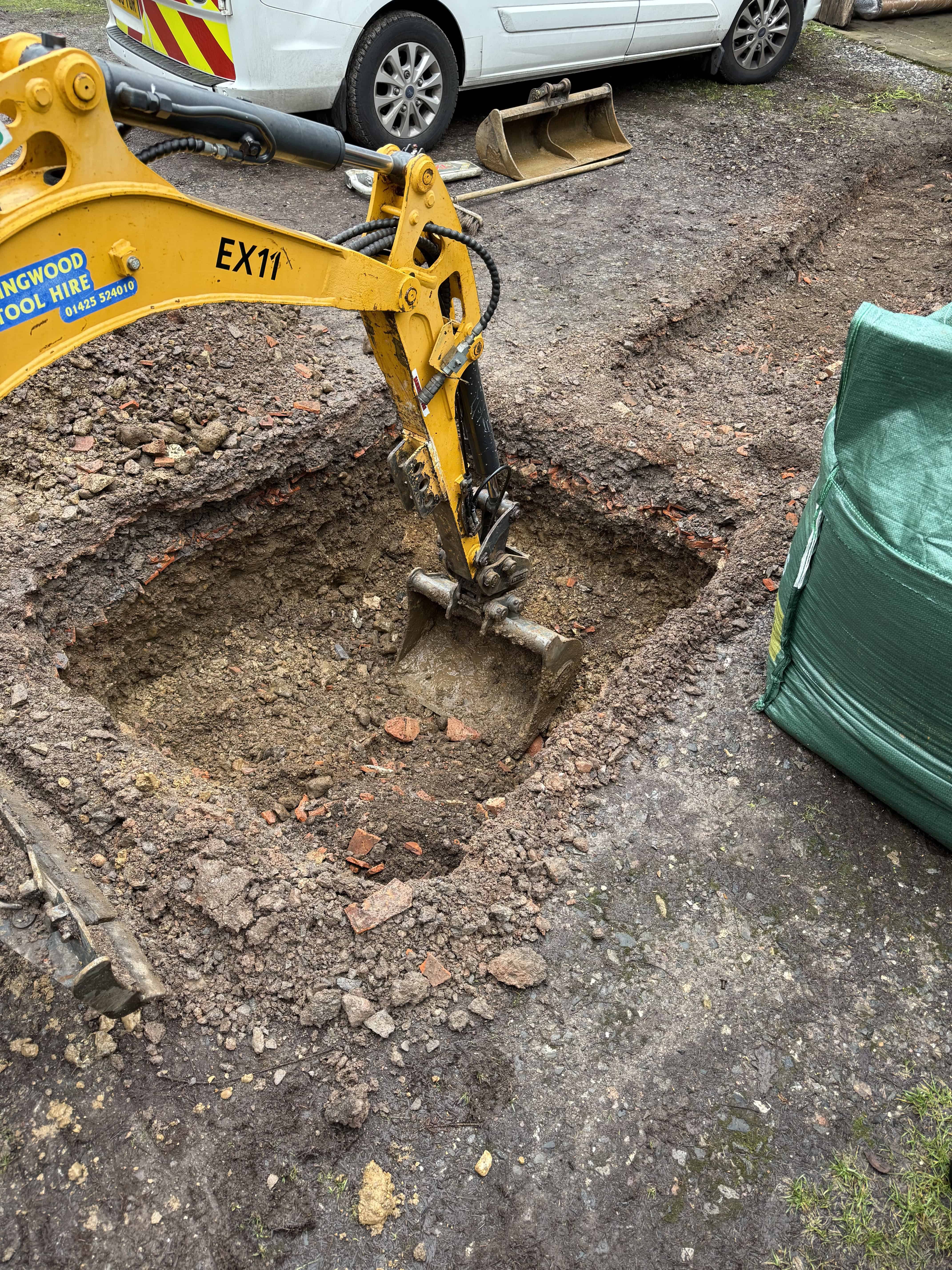 Excavator digging trench for drain installation at a construction site.